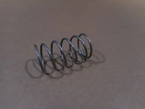 Feder von Remeha, aus Draht in Spiralform, sichtbar auf braunem Hintergrund. Die Feder hat mehrere Windungen, die gleichmäßig verteilt sind.